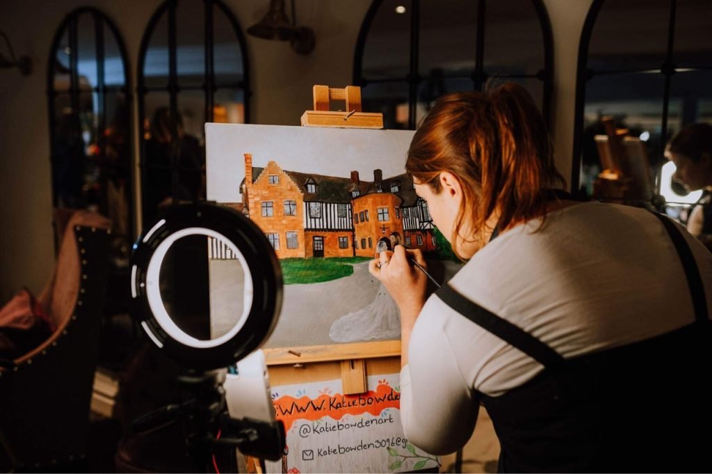 Katie Bowden painting a live wedding canvas in front of an old house