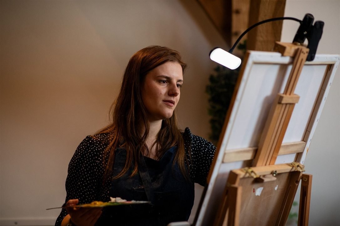 Katie Bowden painting live at an easel, palette in hand