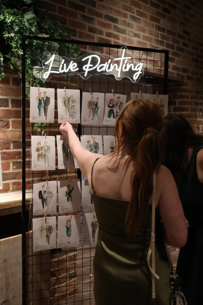 Guest watching watercolour illustrations pegged on a grid beneath a neon Live Painting sign